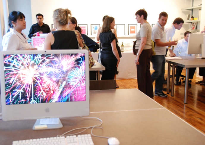 People conversing and reviewing work in a design studio; a computer screen in the foreground displays bursting fireworks.