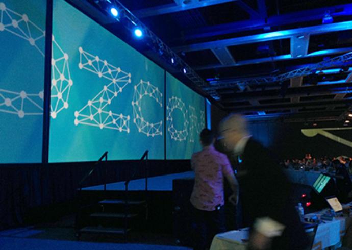 A darkened convention hall with a large screen displaying the MozCon logo.