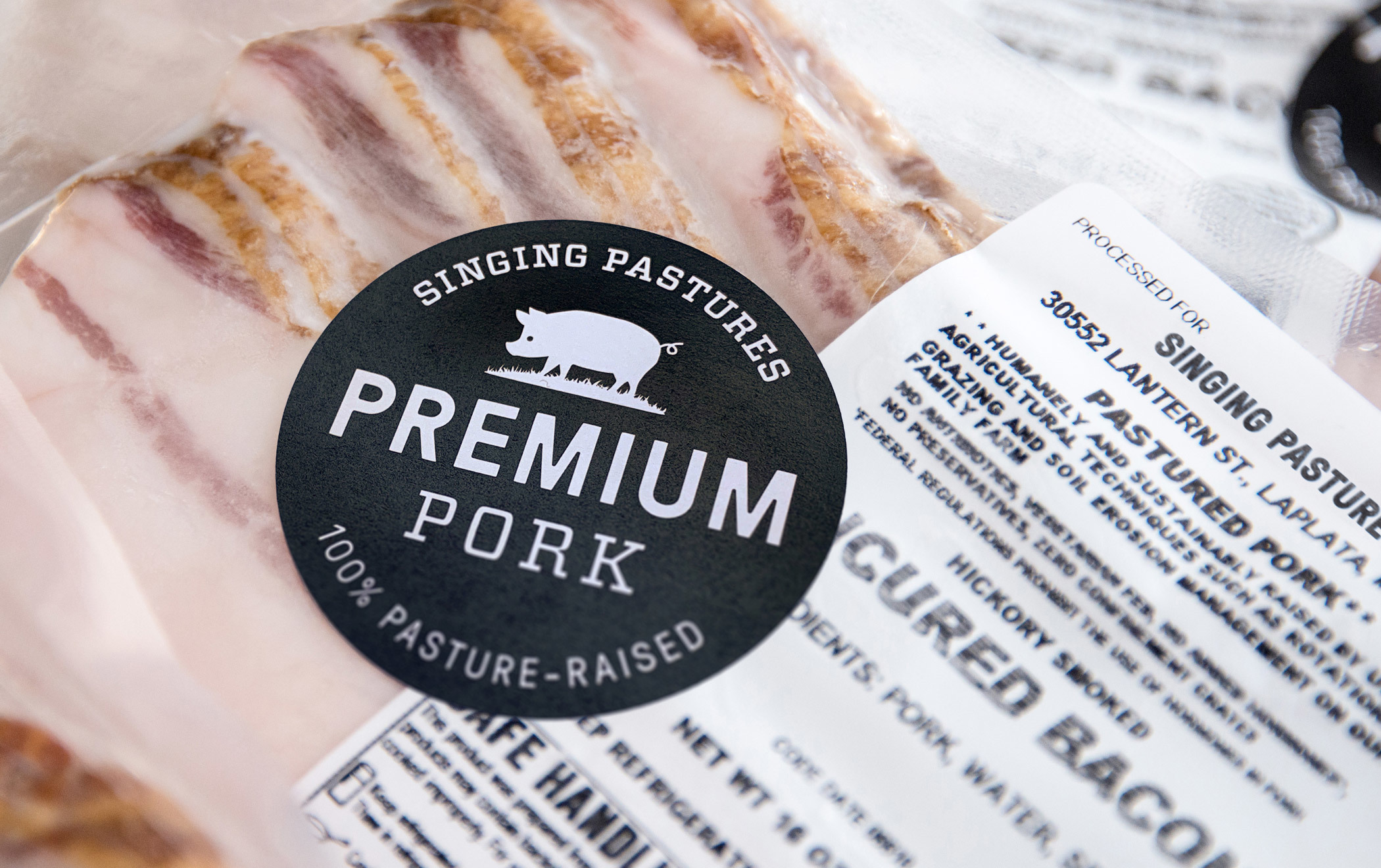 Close up a a Singing Pastures "Premium Pork" sticker affixed to a package of uncured, hickory smoked bacon. 