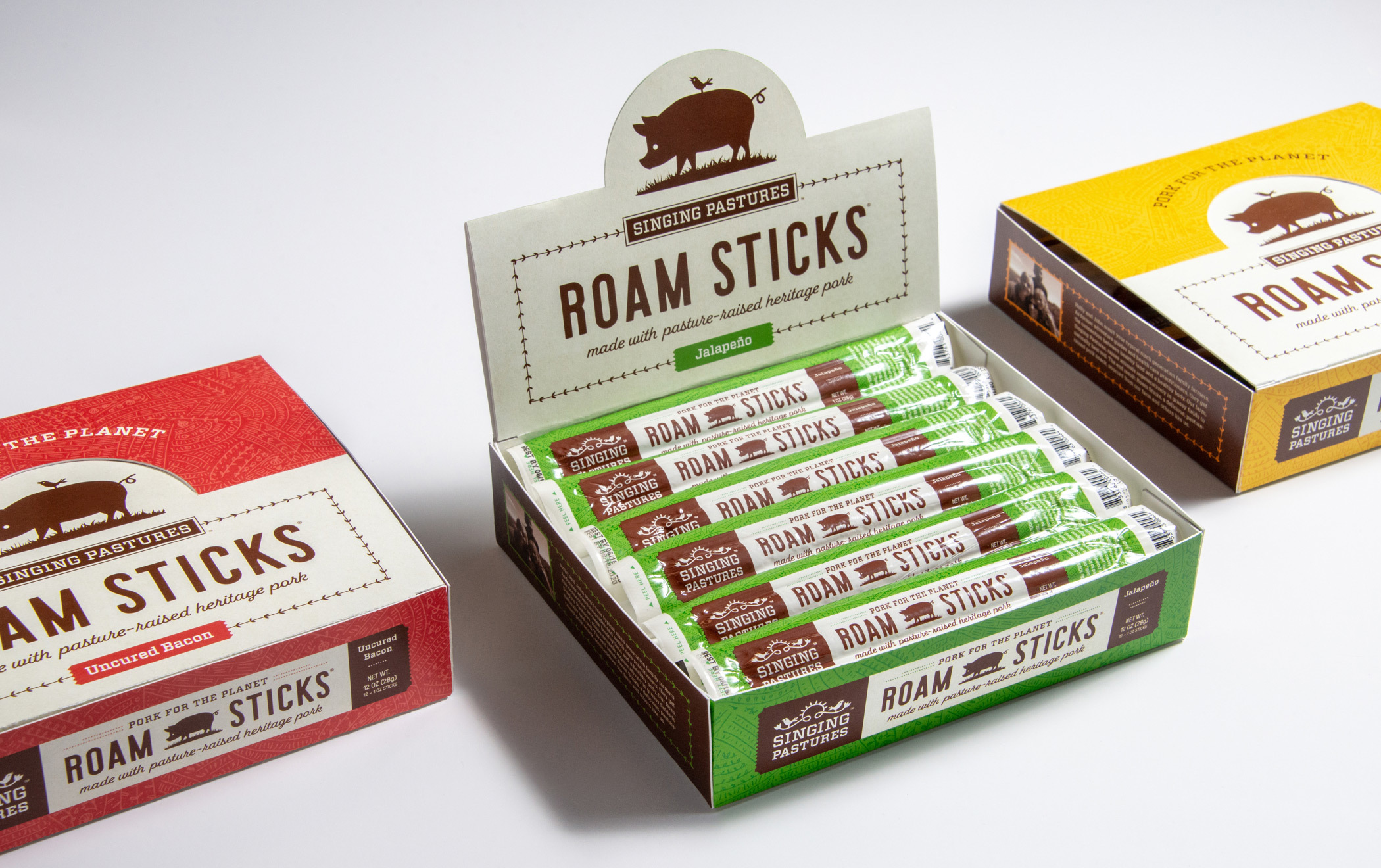 Three boxes of Singing Pastures Roam Sticks snacks arranged on a table. One is open showing individual Roam Stick packages 