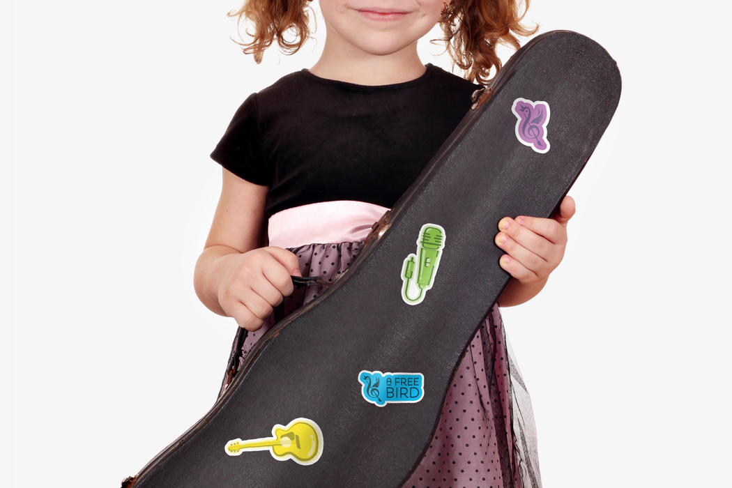 A small child holding a violin case with promotional stickers from the arts organization A Free Bird.