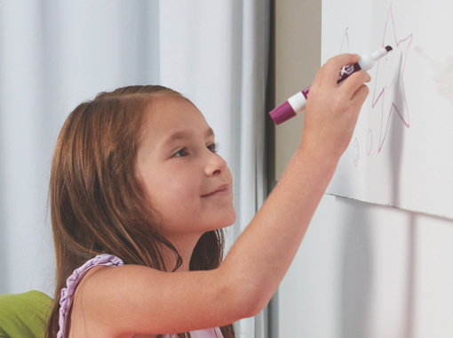 A small child drawing a red star on a large piece of white paper tacked to a wall.