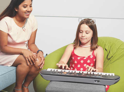 A young woman watches while a young girl plays and electronic keyboard.