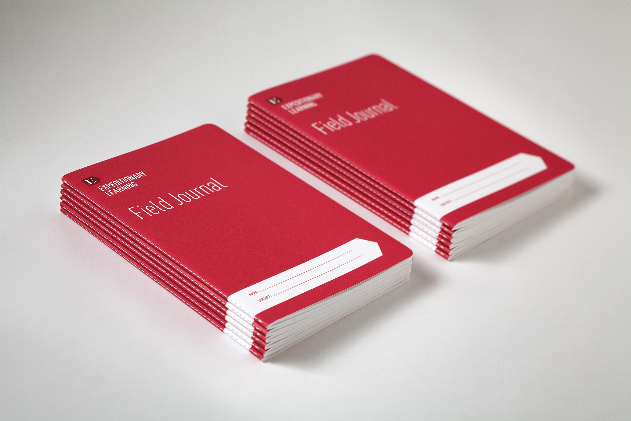 Two stacks of crimson Expeditionary Learning field notebooks.