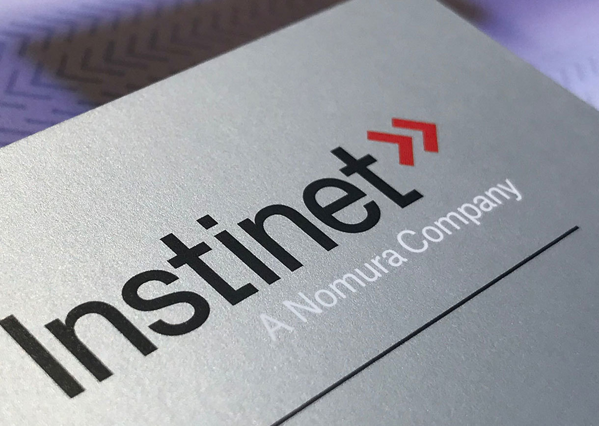 Instinet's logotype and chevron symbol printed on a silver metallic surface.
