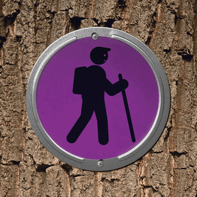 A silhoetted hiker figure on a round trail marker sign. His walking stick transforms into a Singing Pastures Roam Stick.