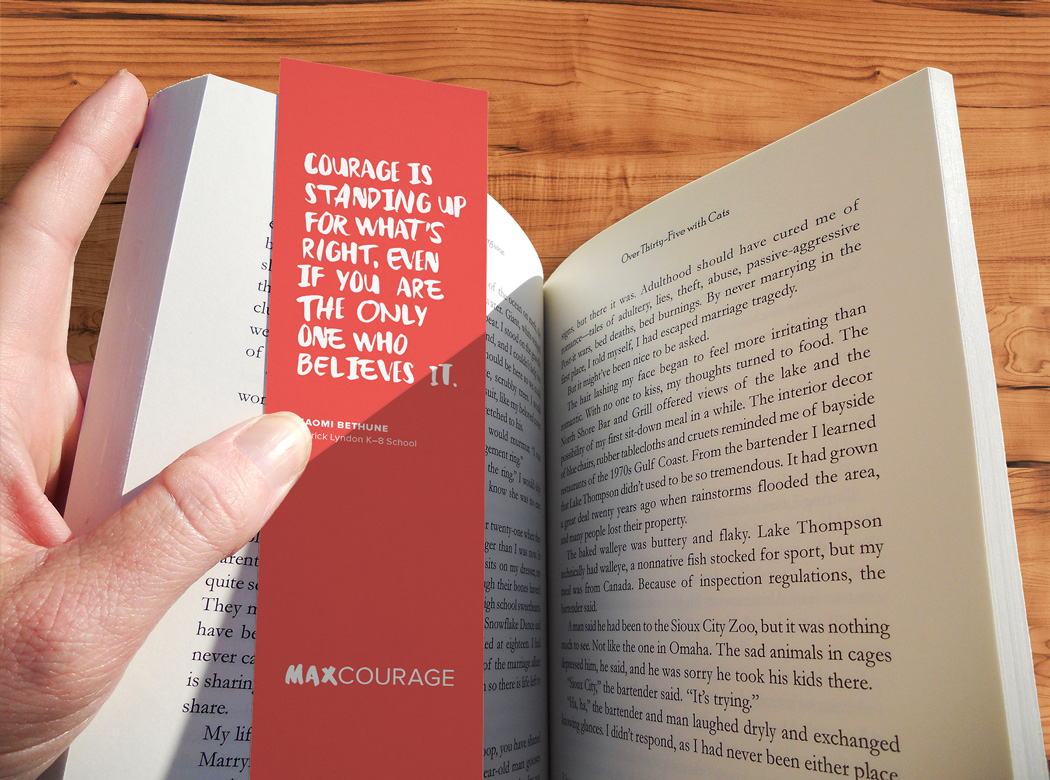 A hand holds the book, "The Courage of Children, Boston and Beyond," with an orange Max Courage branded bookmark.