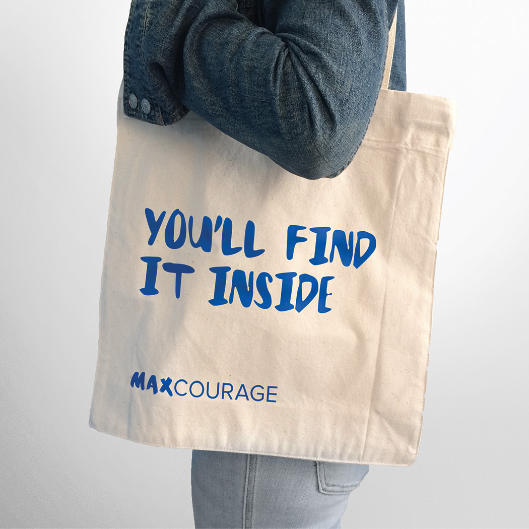 A person holding a Max Courage tote bag with the text, "You'll find it inside."