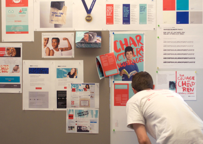 A person leans into to look at designs tacked to the wall for the 2015 Give A Brand design sprint.