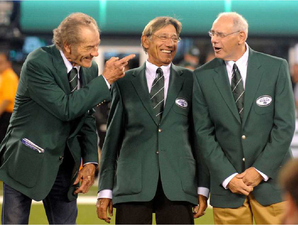 Legendary New York Jets quarterback, Joe Namath, smiles with former teammates wearing Ring of Honor jackets.]