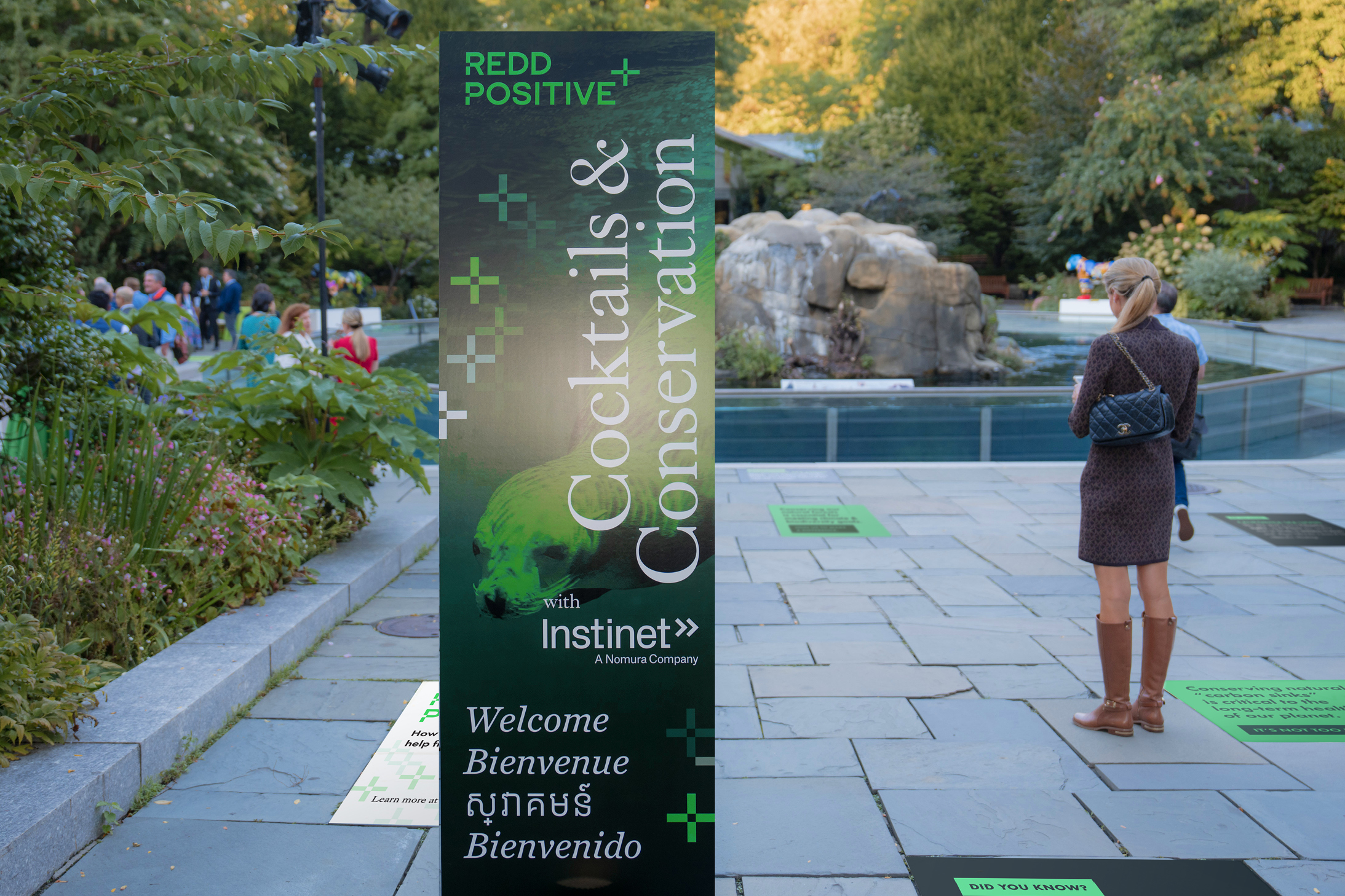 A large vertical sign on a patio at the Central Park zoo greets guests in several languages for the REDD Positive Cocktails and Conservation launch event.